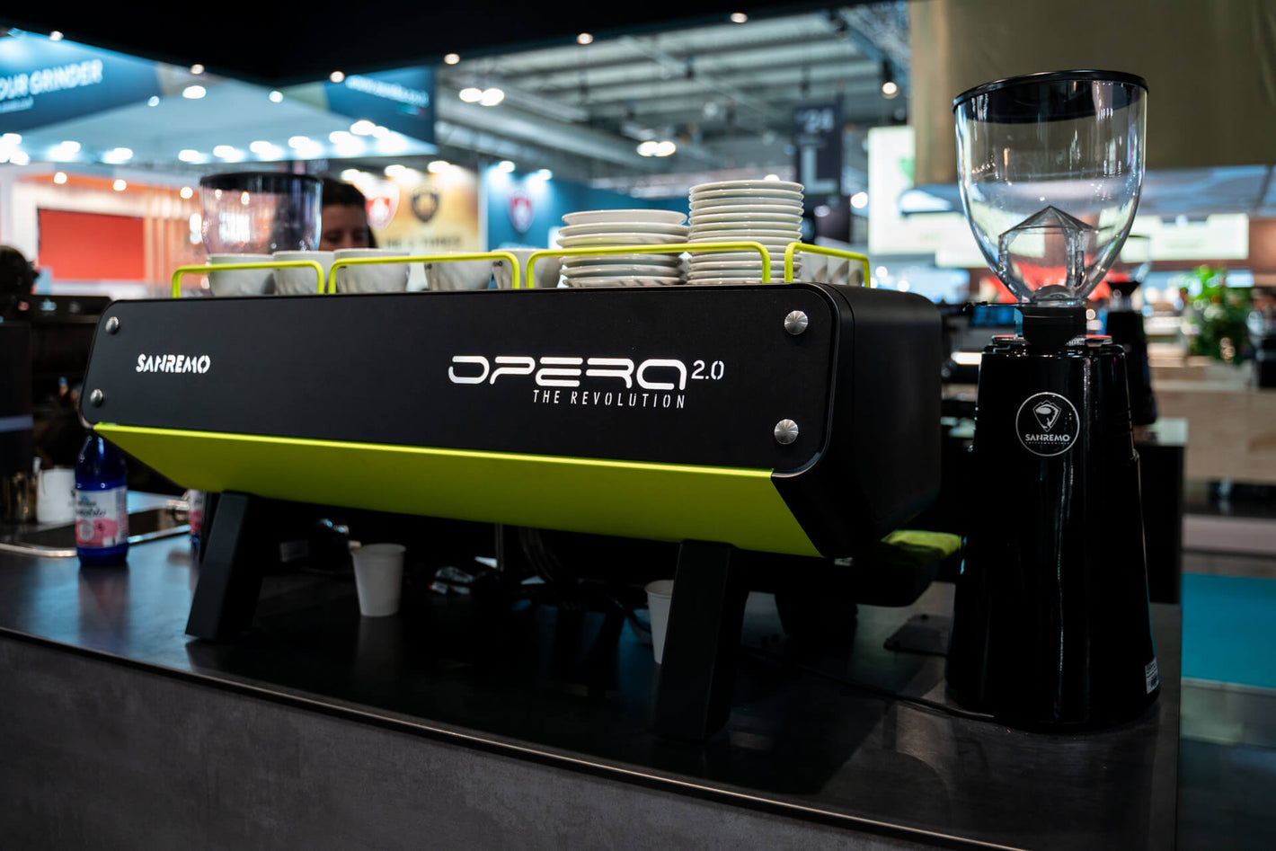 Sanremo Opera Espresso Machine in green and black, and a black Sanremo Coffee Grinder at a Sanremo booth at the coffee equipment event, rear view