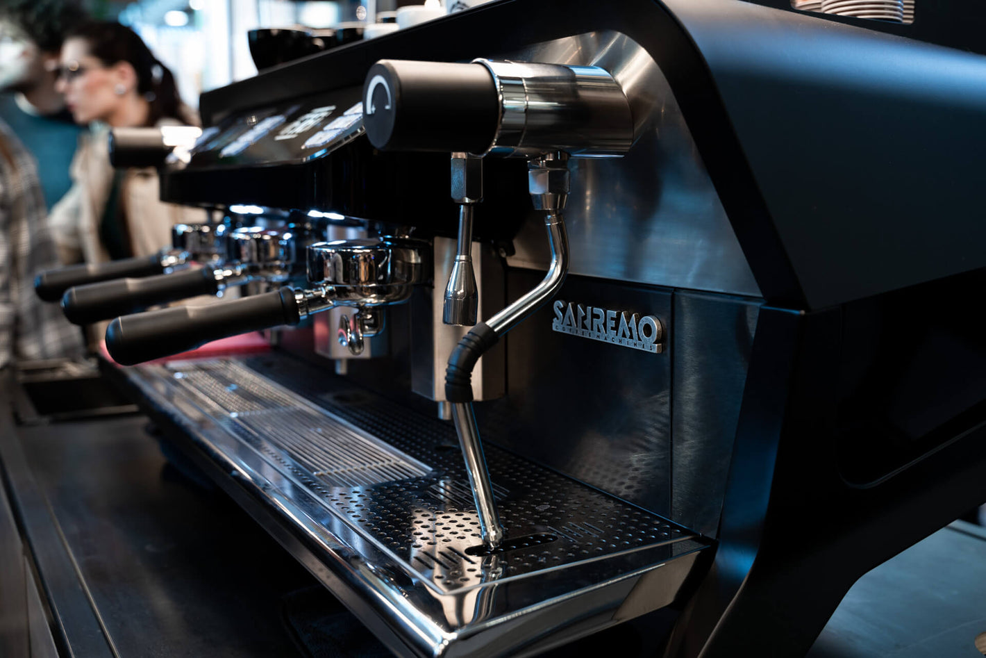 Sanremo F18 3 groups black commercial espresso machine 3/4 view, at a Sanremo booth at a coffee industry event
