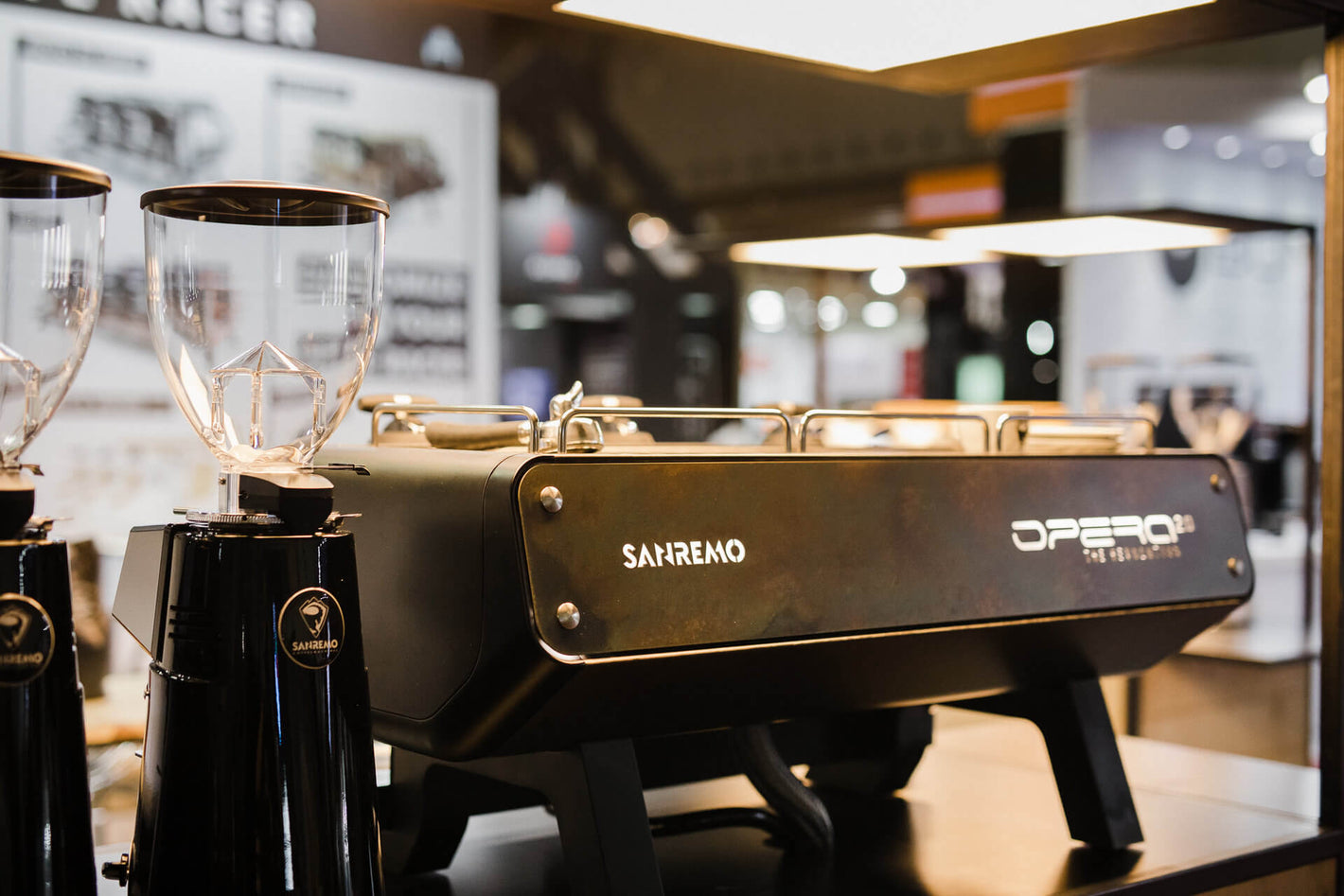 Sanremo Opera 2.0 professional espresso machine and Sanremo Coffee Grinders at coffee industry event on a counter with warm lighting
